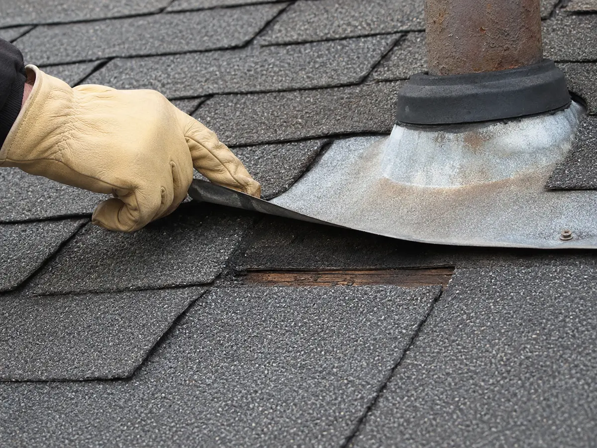 Gloved hand assessing flashing on an asphalt shingle roof